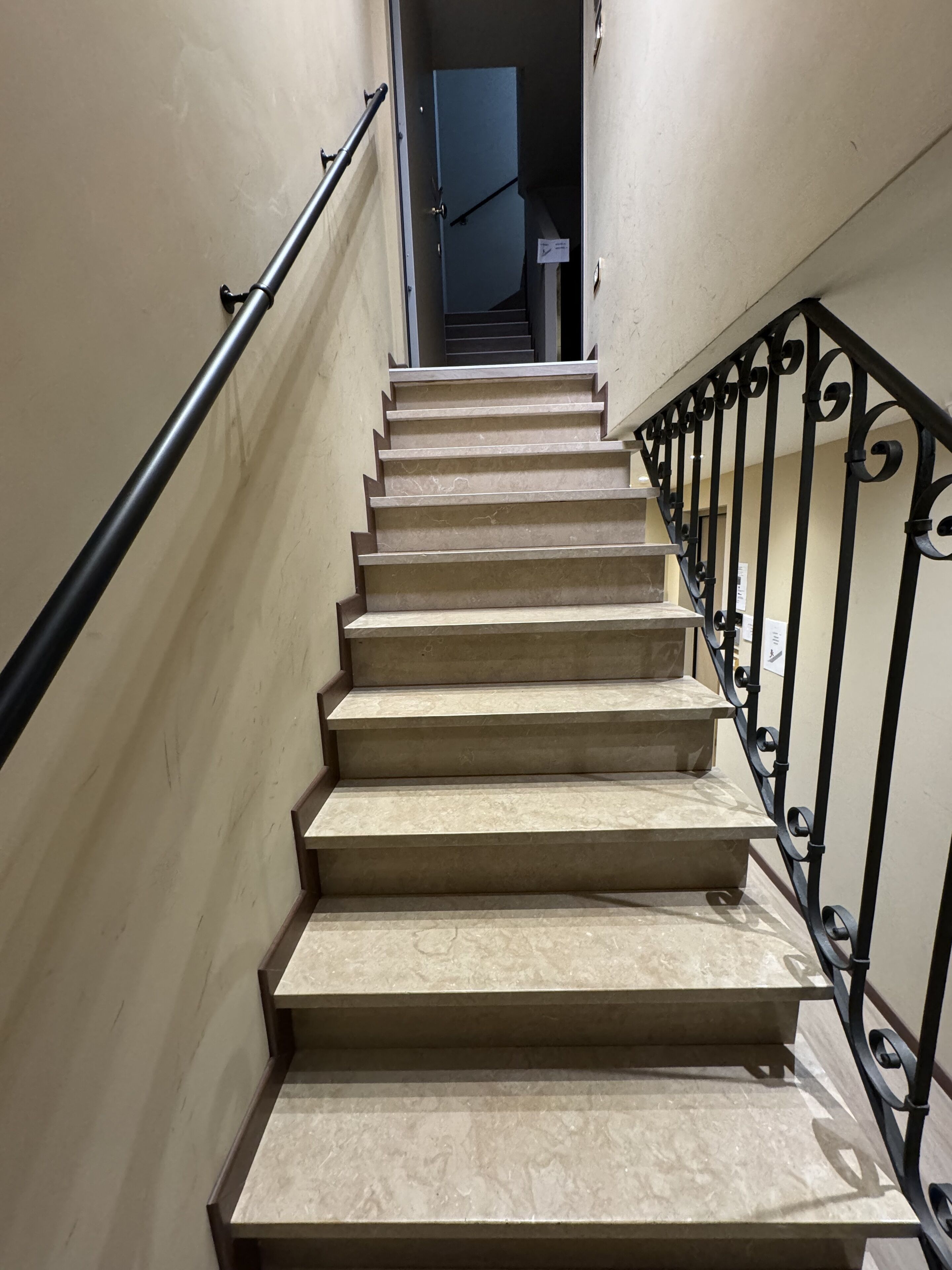 A staircase with beige steps and black metal railings leading to a door at the top.