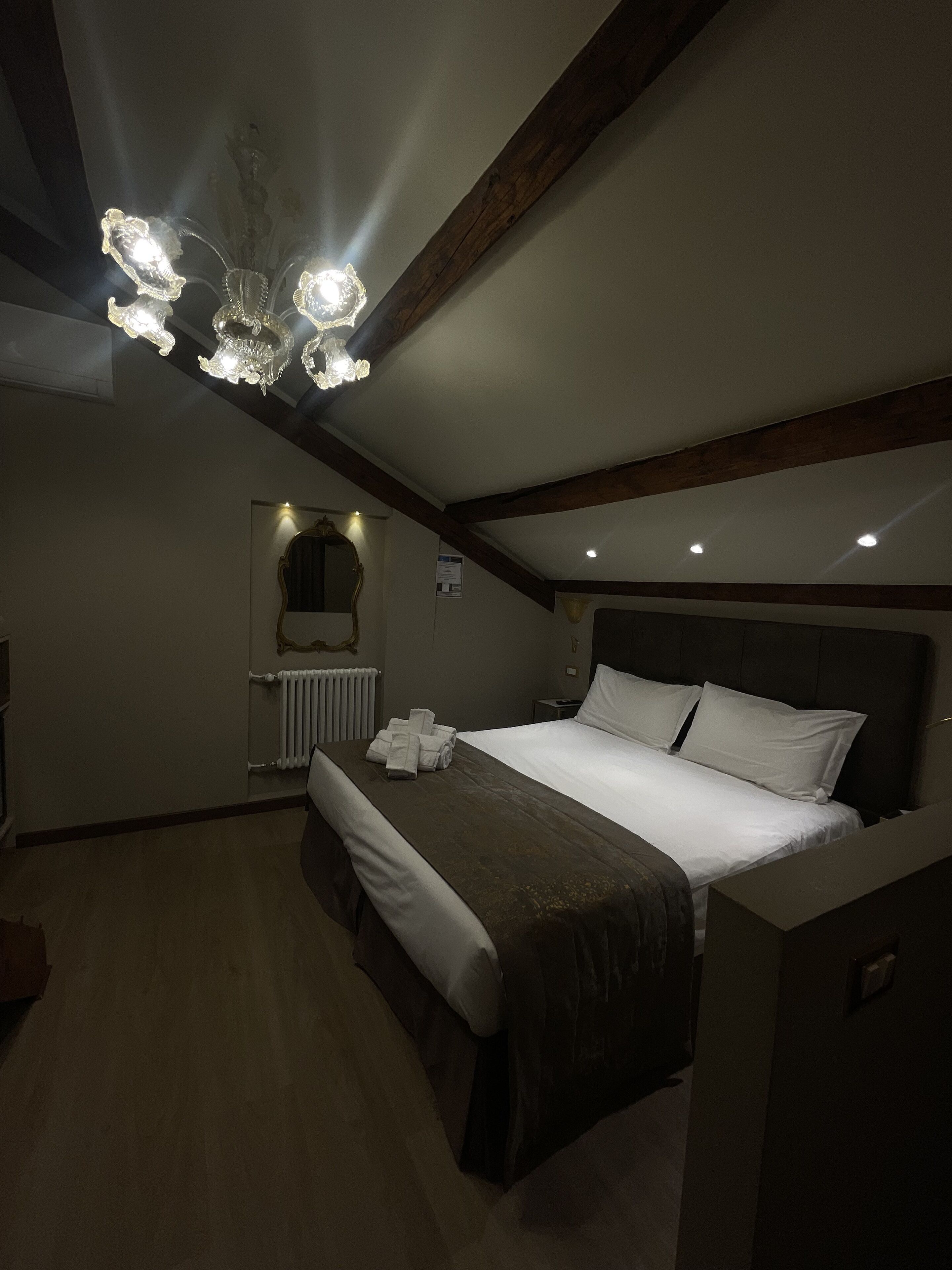 A bedroom with a large bed, a chandelier, a radiator, and a mirror on the wall.