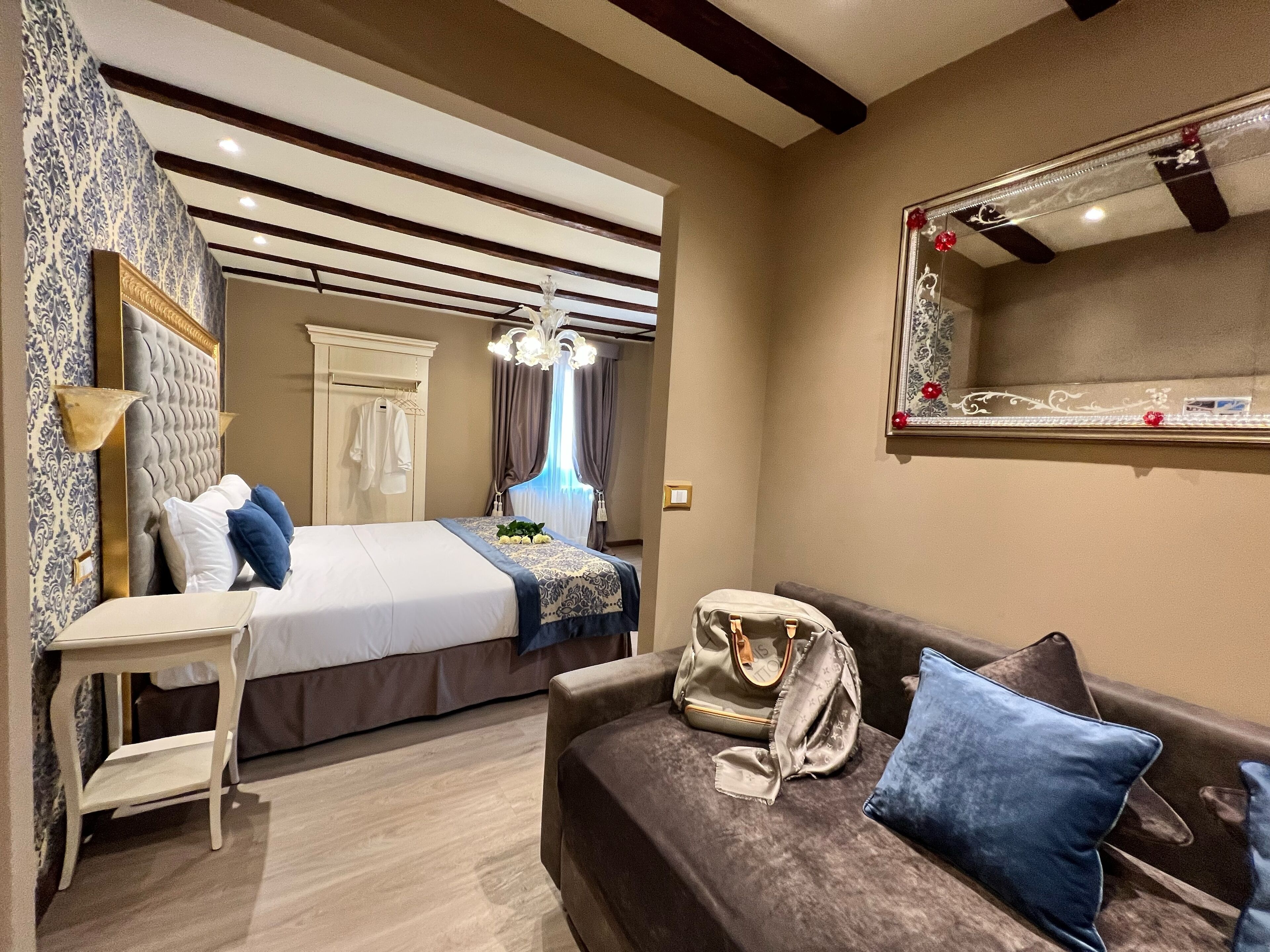 Une chambre à coucher avec un lit, un canapé, une coiffeuse avec un miroir et une valise posée sur le canapé.