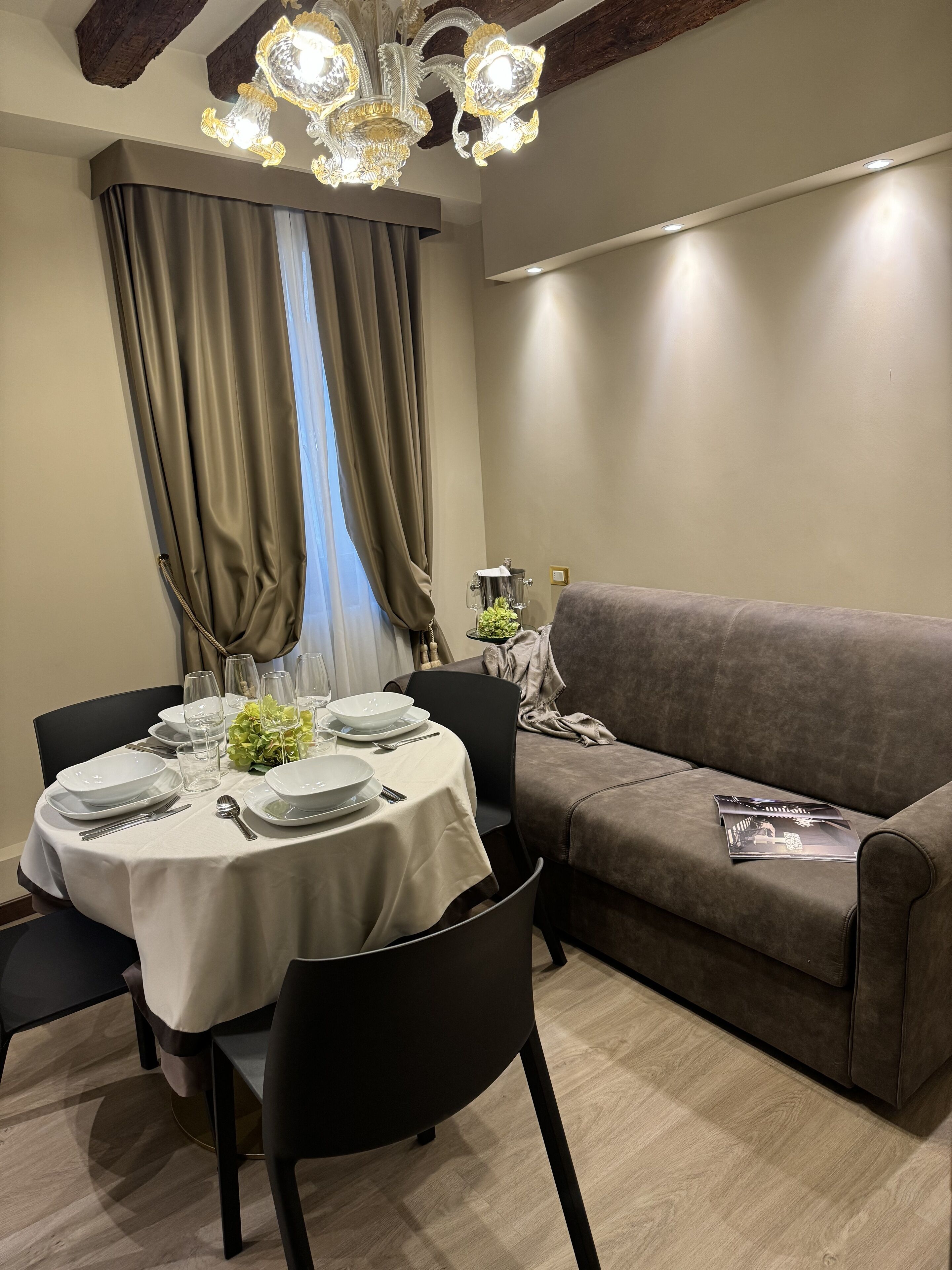A dining area with a round table set for four, a sofa, and a chandelier.