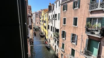 A narrow canal with colorful buildings on either side, a gondola, and people walking on the sidewalk.