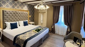 Une chambre à coucher avec un grand lit, un lustre, une petite table avec une chaise et une fenêtre avec des rideaux.