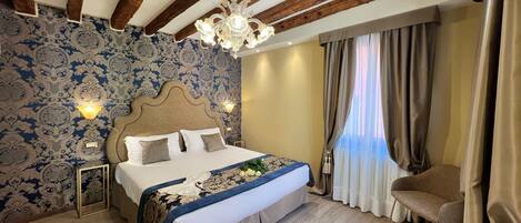 A bedroom with a large bed, a chandelier, a wooden ceiling, patterned wallpaper, and a window with curtains.
