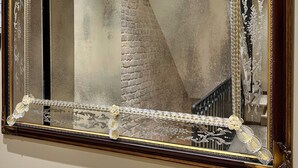 Un grand miroir décoratif à cadre doré, dans lequel se reflètent un escalier et un mur de briques.