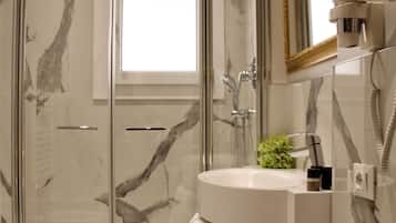 A modern bathroom with a glass-enclosed shower, a white sink, and a mirror with a gold frame.