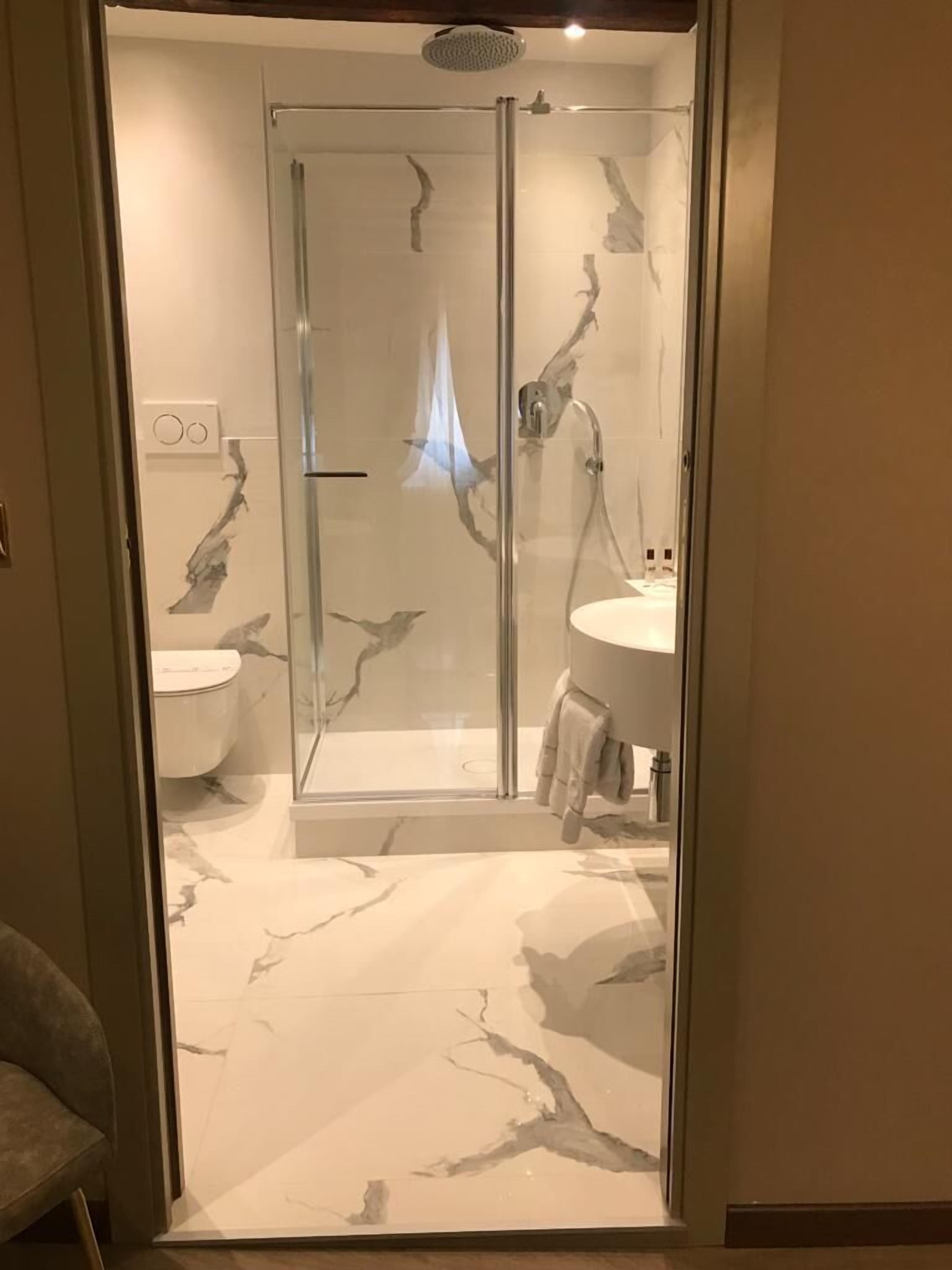 A modern bathroom with a glass-enclosed shower, a white marble floor, and a visible toilet.