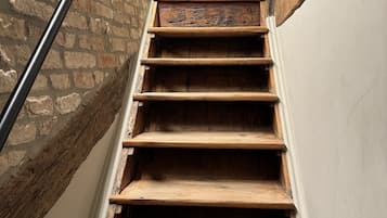 A wooden staircase with a metal handrail, leading to a room with a white wall and a hanging light fixture.