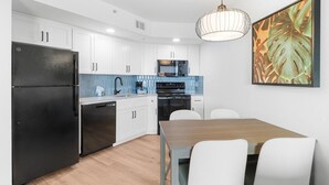Una cocina moderna con armarios blancos, un refrigerador negro, un microondas y un comedor con mesa de madera y sillas blancas.