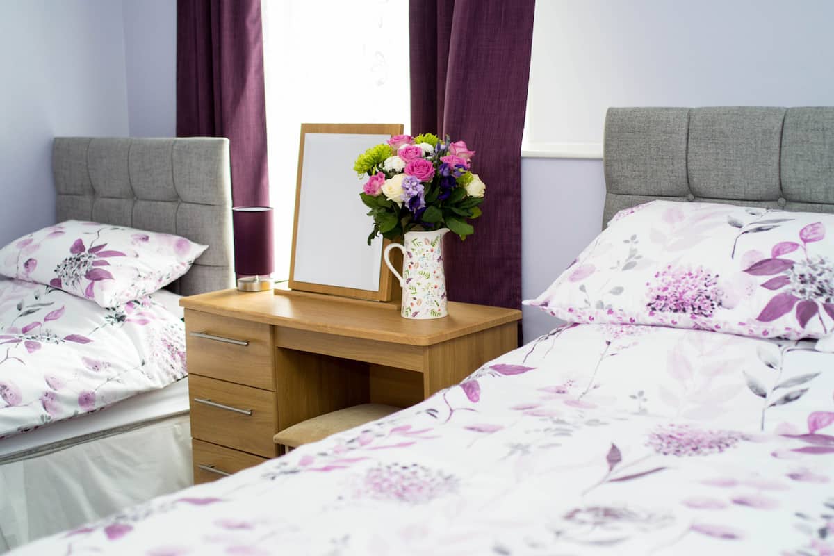 Een slaapkamer met twee bedden, een houten bureau, een spiegel en een bloevas.