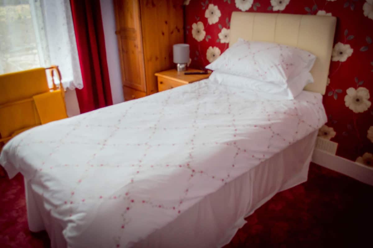 Een bed met een witte spreideken in een kamer met bloemenbehang en een houten hoofdeinde.