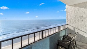 Un balcon avec vue sur l’océan, une balustrade en verre et deux chaises.