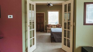 A hallway leading to a bedroom with a bed, a window, and a door.