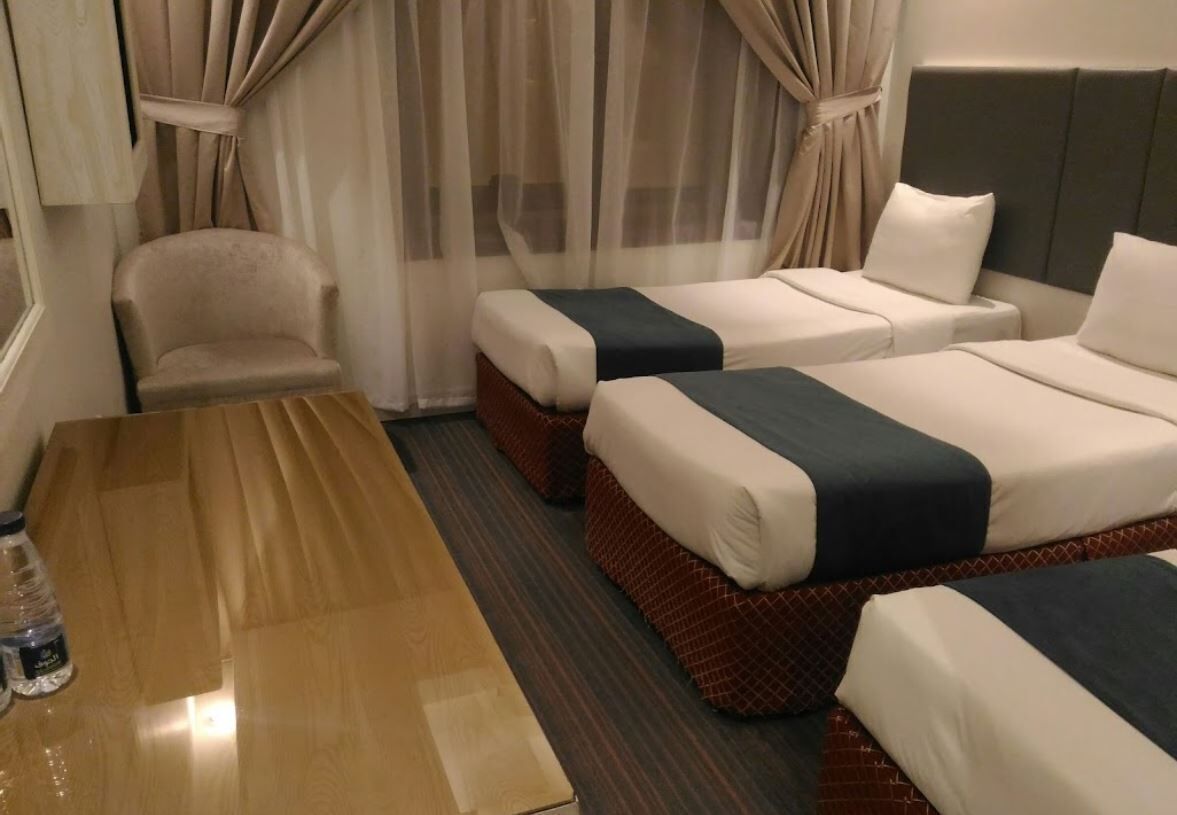 A hotel room with two beds, a wooden table, a chair, and a window with curtains.
