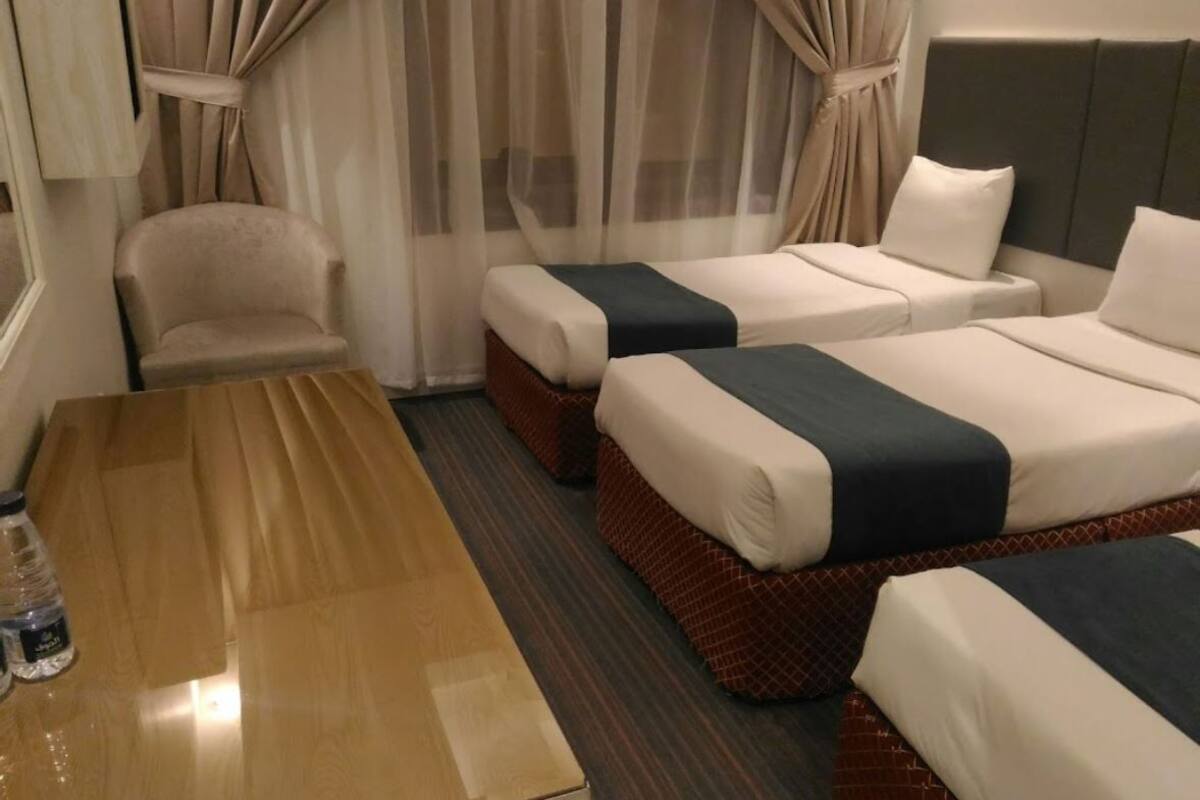 A hotel room with two beds, a wooden table, a chair, and a window with curtains.