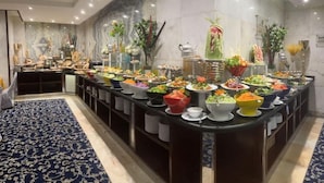 A buffet setup with various food items and decorative plants. - Maysan Al Mashaer Hotel (Makkah)