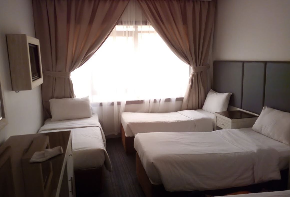 A hotel room with two single beds, a nightstand, a wooden dresser, and a window with curtains.