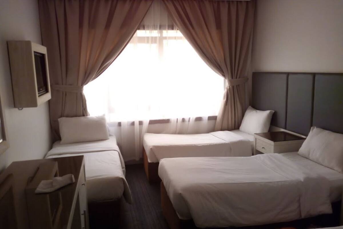 A hotel room with two single beds, a nightstand, a wooden dresser, and a window with curtains.