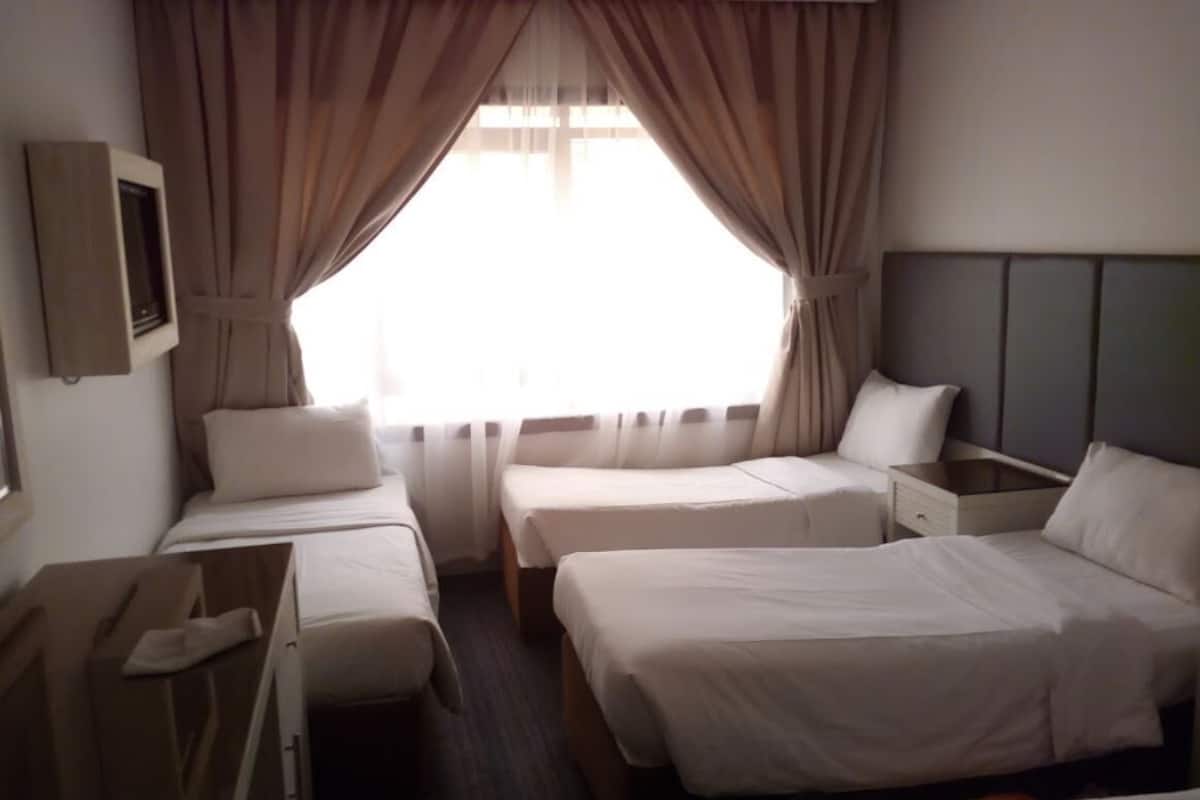Une chambre d’hôtel avec deux lits simples, une table de chevet, une commode en bois et une fenêtre avec des rideaux.