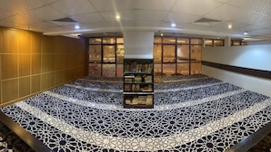 A circular reading area with a patterned floor, a central bookshelf, and a view of the outside through large windows. - Maysan Al Mashaer Hotel (Makkah)