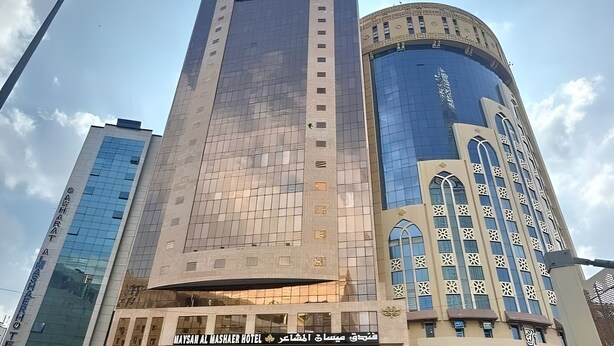 A hotel with a modern design, featuring a prominent glass facade and a traditional architectural style with arched windows. - Maysan Al Mashaer Hotel (Makkah)