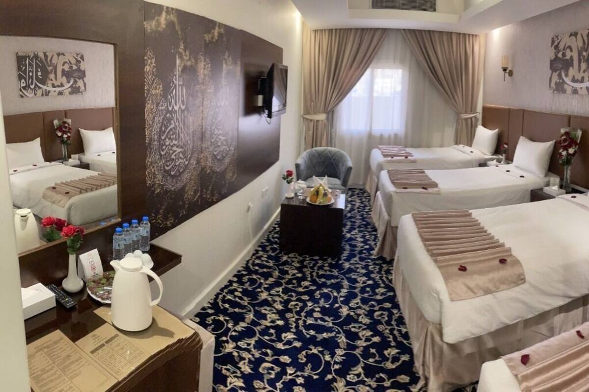 A hotel room with four beds, a desk with a vase of flowers, a coffee maker, and a large mirror.
