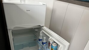 Un réfrigérateur blanc doté d’un compartiment congélateur, contenant deux bouteilles d’eau et une canette de soda.