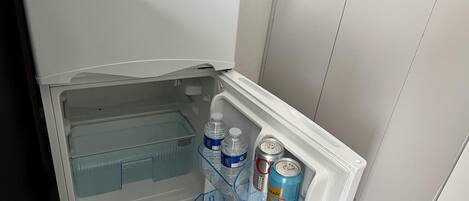 A white refrigerator with a freezer compartment, containing two water bottles and a can of soda.