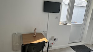 Une pièce avec une table en bois, une chaise noire, un téléviseur fixé au mur et une fenêtre donnant sur un garage.