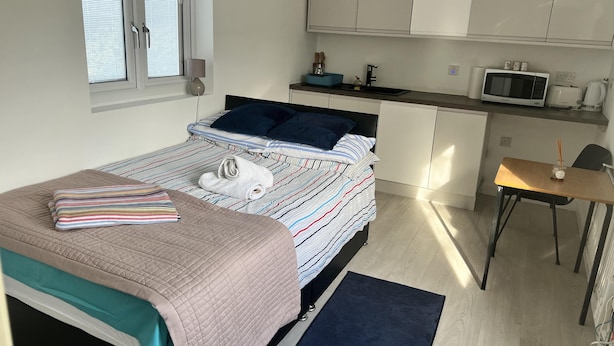 Une chambre compacte comprenant un lit, une table de chevet et une petite kitchenette.