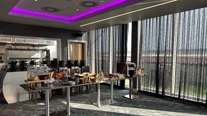 Et moderne receptionområde med en receptionsdisk, kaffestation og udsigt til det fri gennem store vinduer.