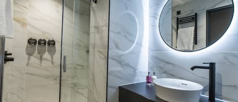 A modern bathroom with a glass-enclosed shower, a round mirror, and a white sink with a black faucet.