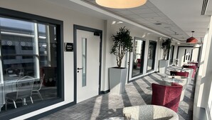 Et hotelkærestemil med et siddeområde med runde borde og røde stole, en potteplante og et skilt der viser 'McCroe Suite 3'.