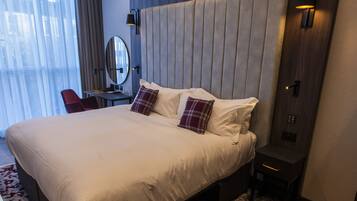 Habitación de hotel moderna con una cama grande, un escritorio, una silla, un espejo y una lámpara de pared.