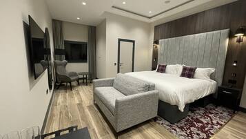 A modern hotel room with a large bed, grey upholstered armchair, and a small table with glasses.