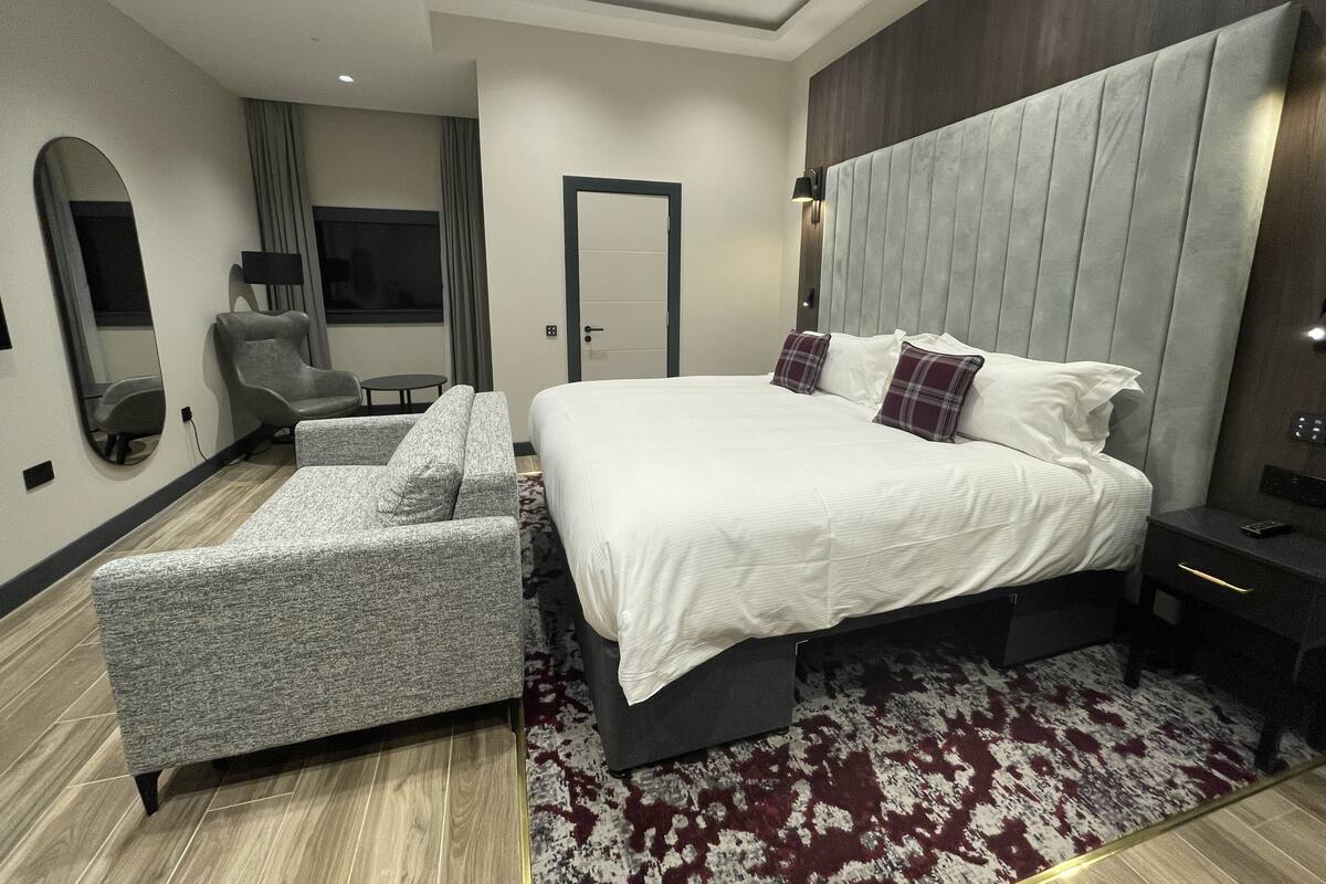 A modern bedroom with a large bed, a grey sofa, a small table, and a mirror.