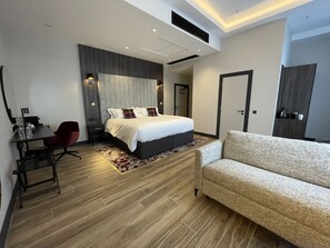 Ein modernes Hotelzimmer mit Bett, Schreibtisch, einem roten Sessel, einer Couch und Holzboden.