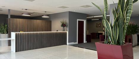 A modern reception area with a wooden reception desk, a potted plant, and a red accent wall.