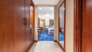 A hotel hallway leading to a room with a blue carpet, wooden doors, and a bed with white linens. - Shaza Regency Plaza (Madinah)
