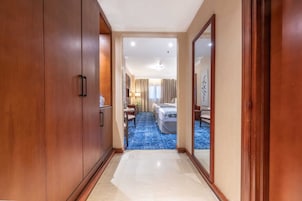 A hotel hallway leading to a room with a blue carpet, wooden doors, and a bed with white linens.