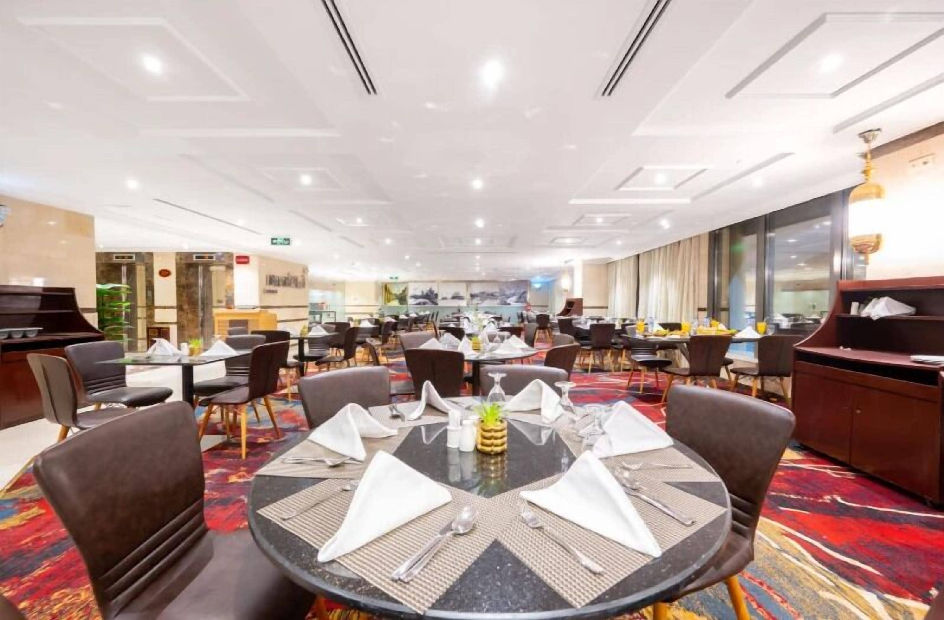 Un comedor amplio con mesas redondas dispuestas para cuatro personas, con servilletas, cubiertos y un centro de mesa.