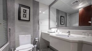 A modern bathroom with a toilet, bidet, and sink. There are framed pictures on the wall and a large mirror above the sink. - Shaza Regency Plaza (Madinah)