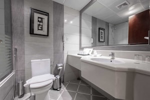 A modern bathroom with a toilet, bidet, and sink. There are framed pictures on the wall and a large mirror above the sink.