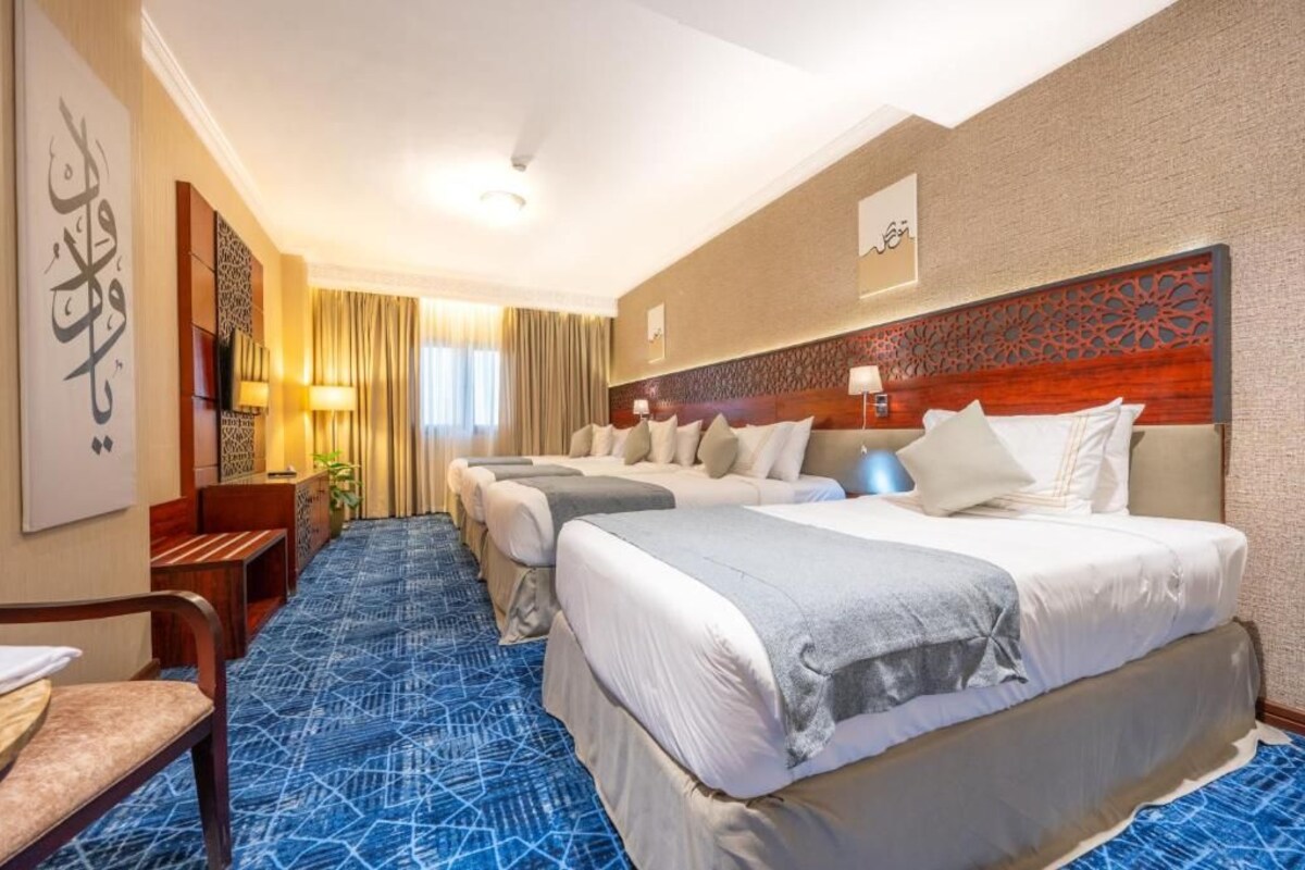 A hotel room with three beds, a blue patterned carpet, a wooden headboard, and a wall with calligraphy.