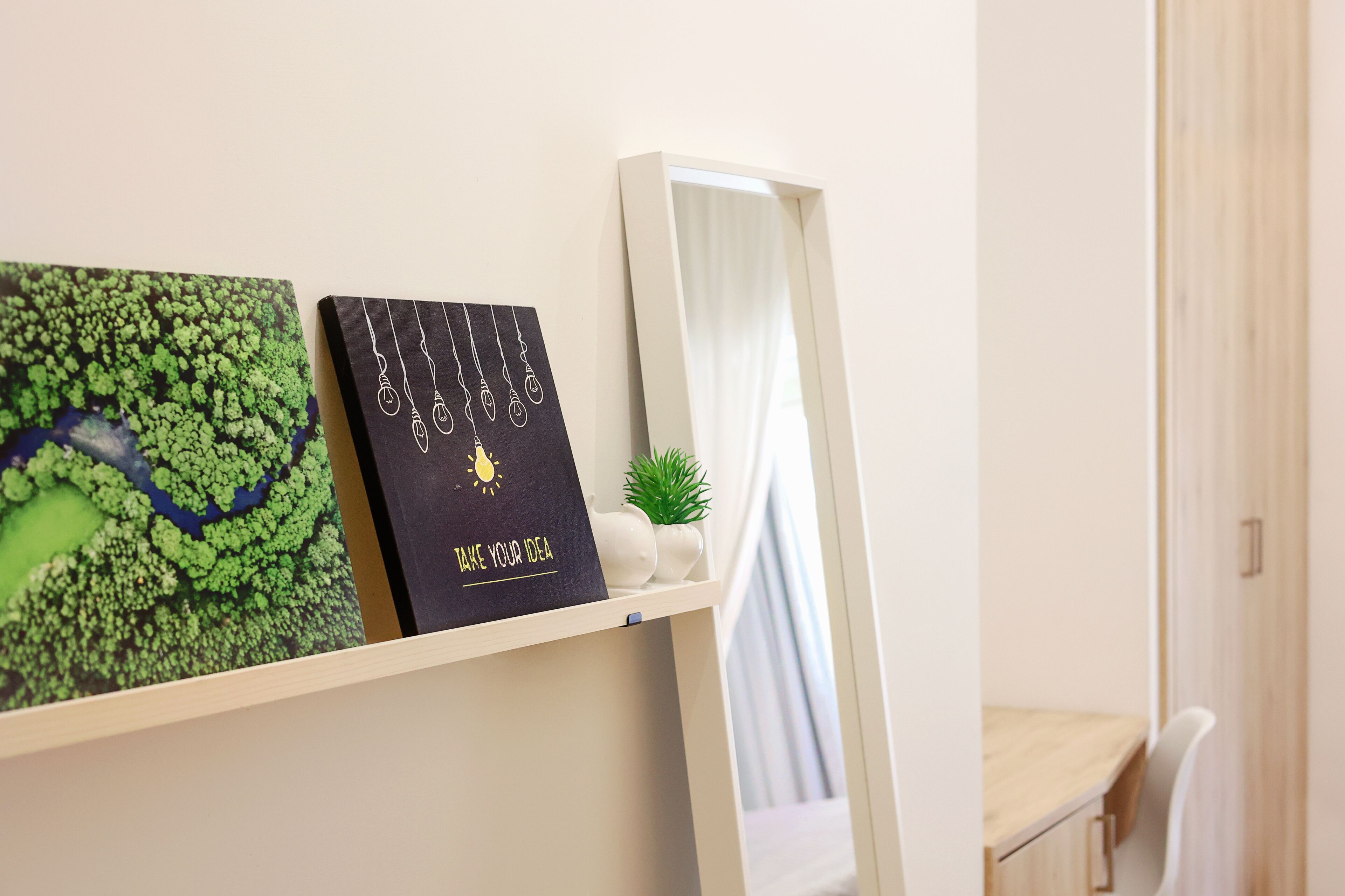 Una habitación con un escritorio blanco, un espejo, una estantería con una planta y un cuadro enmarcado.