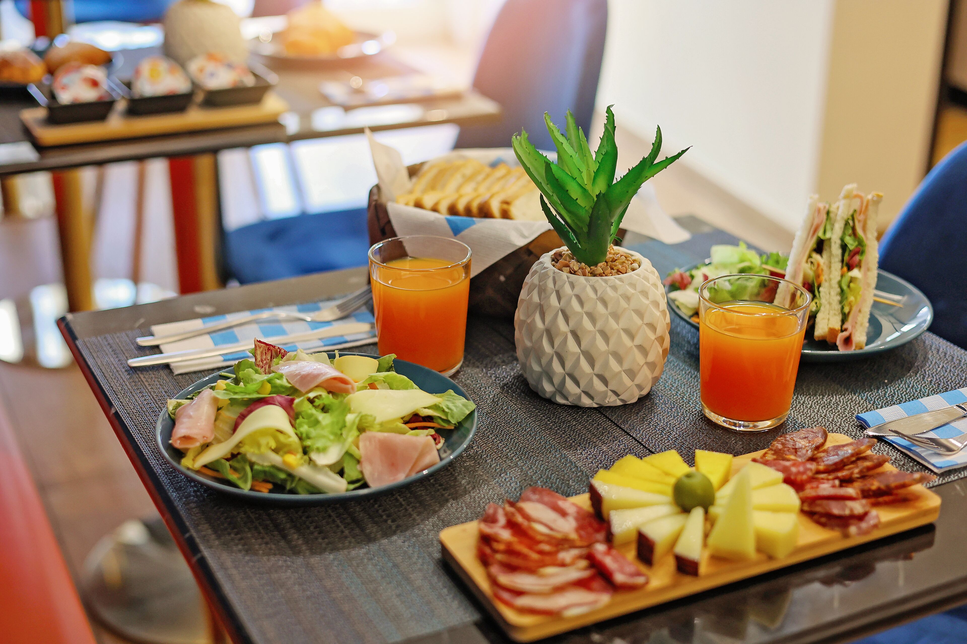 Una mesa de desayuno con ensalada, fruta, embutidos y zumo de naranja.