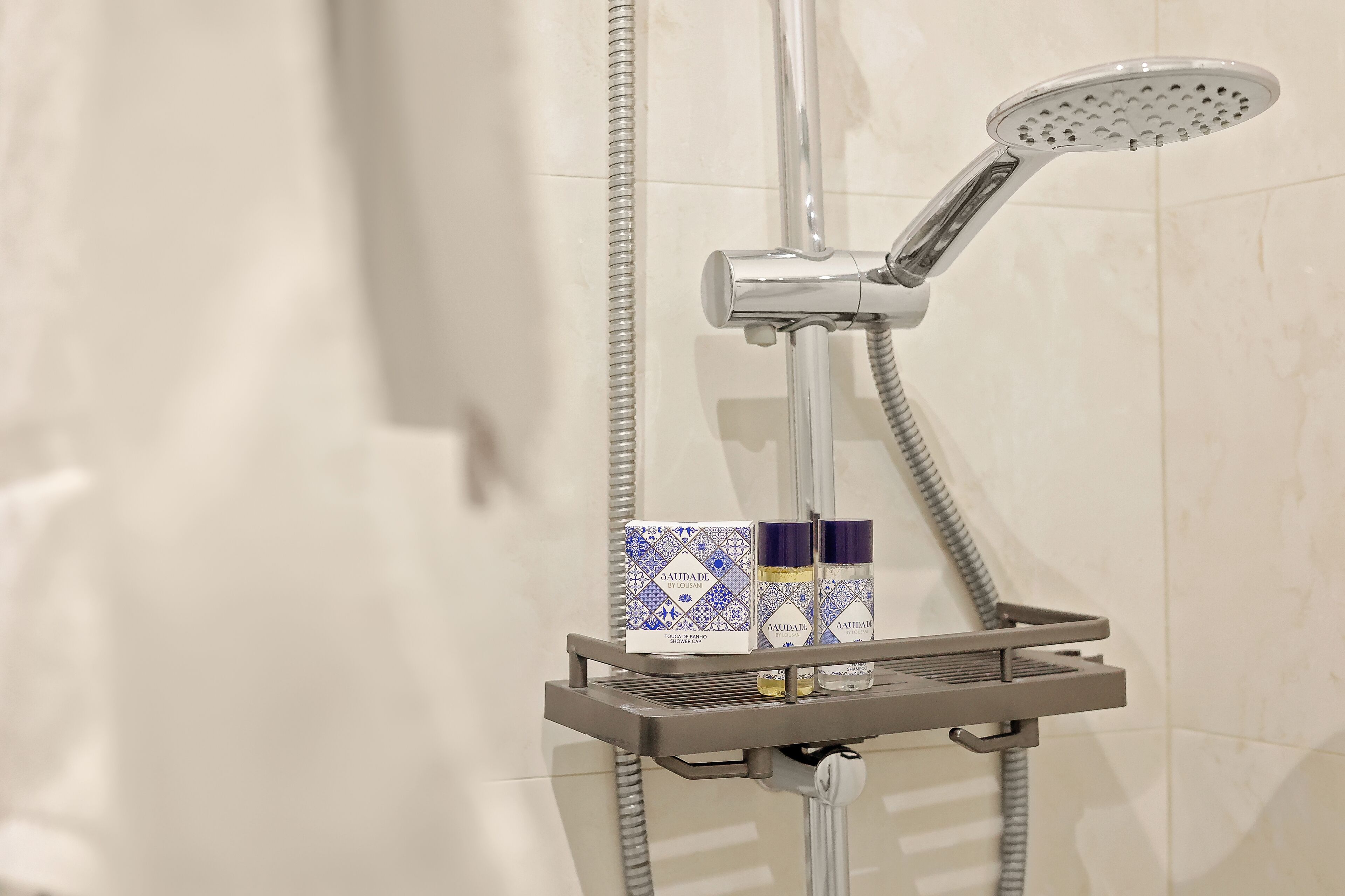A shower with a handheld showerhead and a wall-mounted one, a grey shower tray, and two bottles of SAUDADE body wash on the tray.
