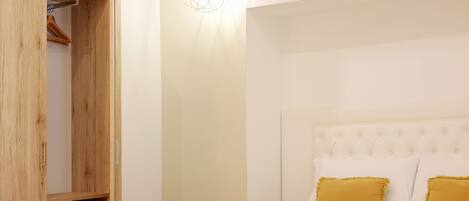 A bedroom with a wooden wardrobe, a bed with white and mustard pillows, and a hanging light fixture.