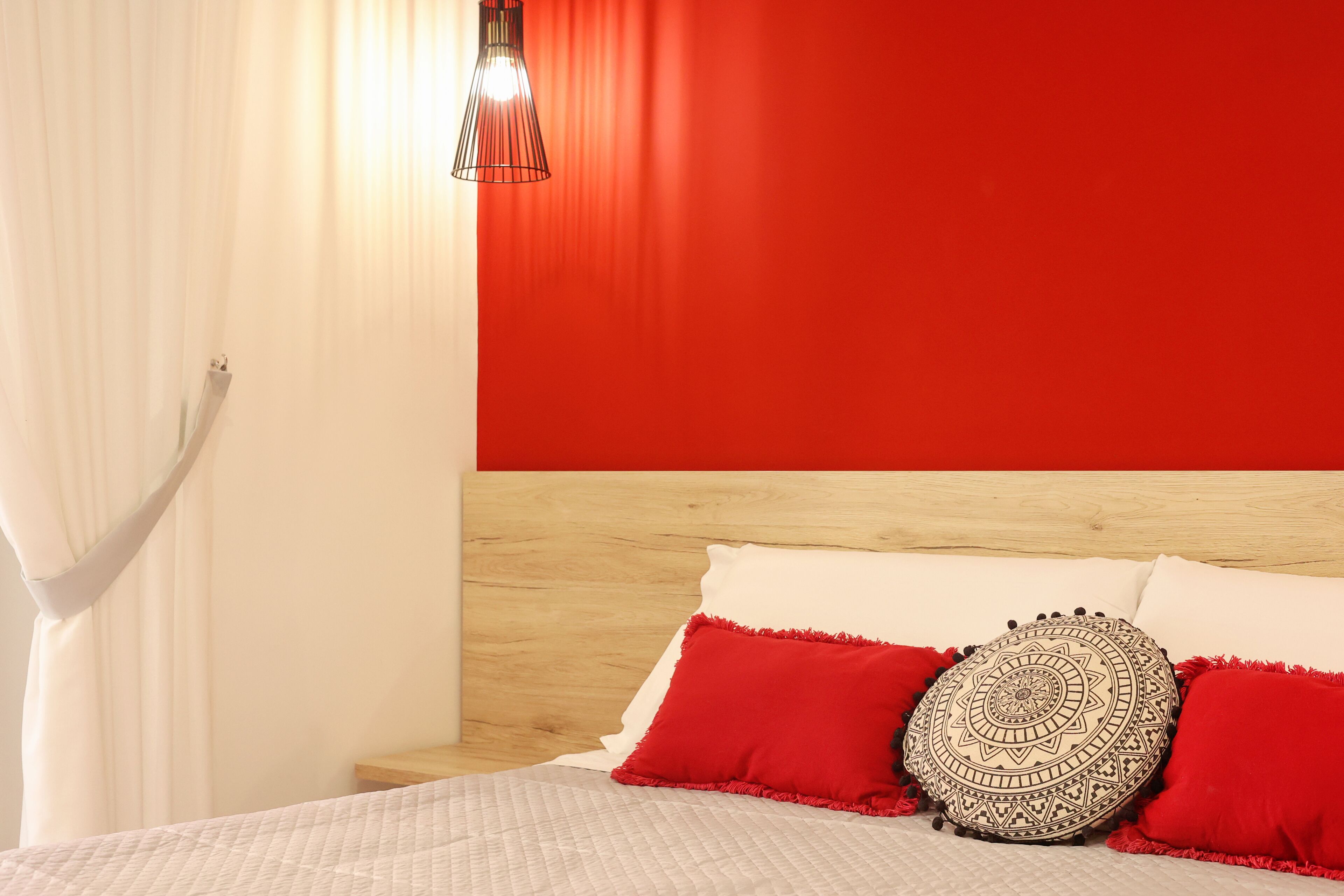 A bedroom with a red wall, a wooden headboard, and a bed with white and red bedding.