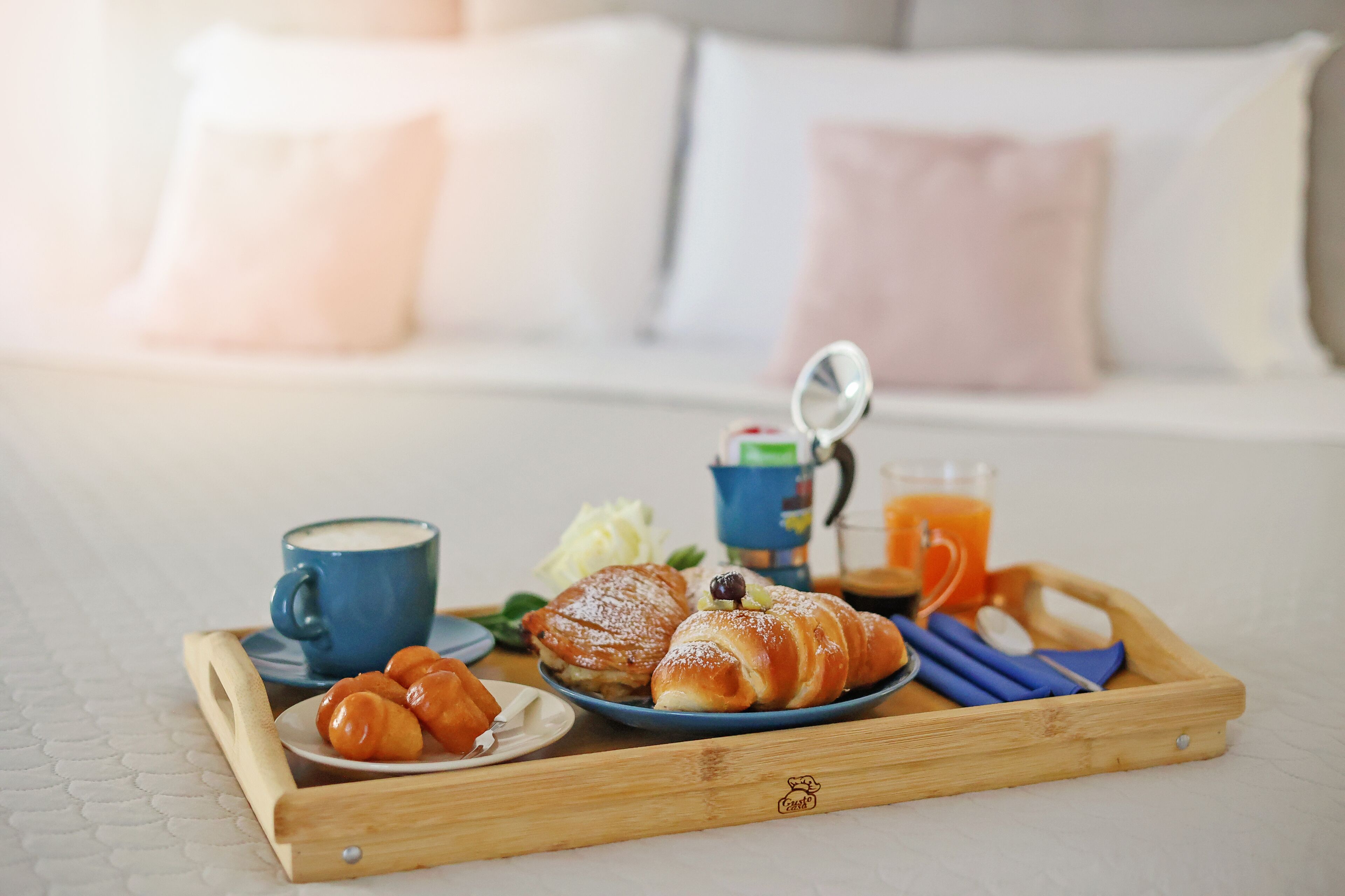 A breakfast tray with pastries, a cup, and a glass of orange juice on a bed.