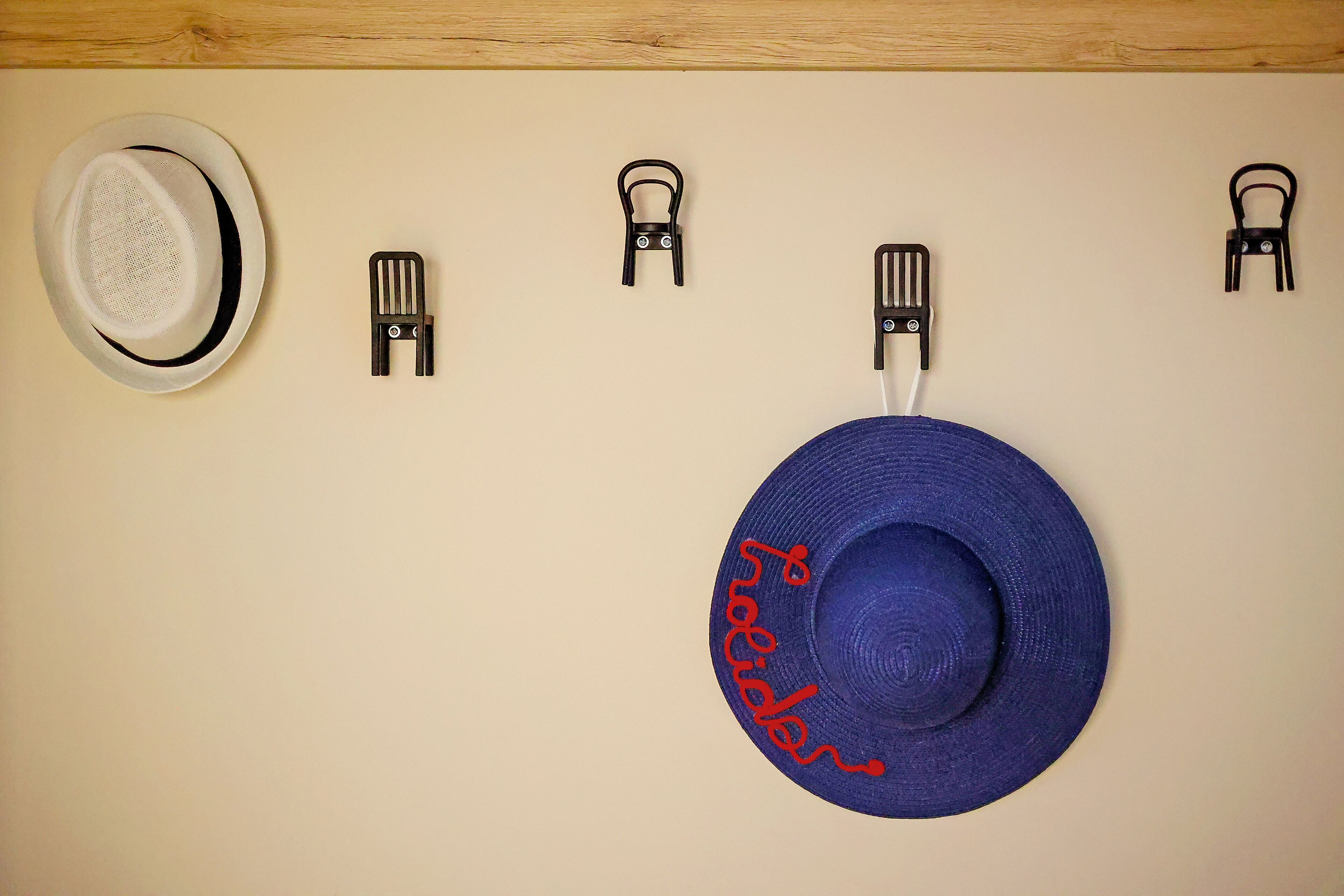 Eine Wand mit einem weißen Hut und einem blauen Hut, auf dem 'Holiday Inn' eingestickt ist, beide an Haken hängend.